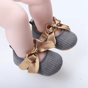 Vista detallada de zapatos de bebé grises con elegantes y grandes lazos de satén dorado