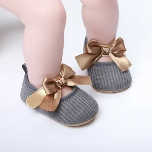 Primer plano de zapatos de princesa para bebé con lazo dorado y textura de punto gris.