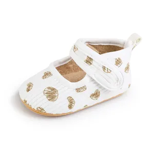 Close-up of white baby walker shoe with gold heart pattern and Velcro strap detail