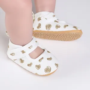 Detail view of white baby walking shoes with gold heart prints and non-slip soles.