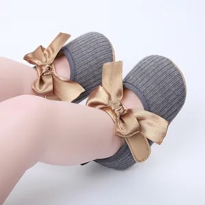 Primer plano de zapatos de princesa grises para bebé con elegantes lazos de satén dorado