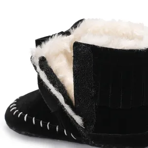 Close-up detail of black baby tassel boots with warm white fur lining and velcro strap.