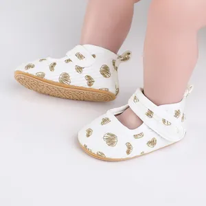 Close-up of white baby walking shoes with gold heart patterns and T-strap closure