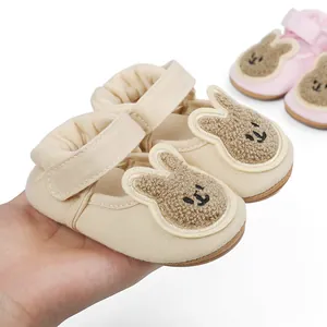 Close-up of beige infant pre-walker shoes with cute plush rabbit patch and strap.