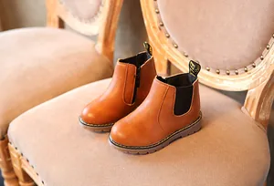 Detalle de cerca de botines Chelsea para niños en cuero marrón sobre una silla