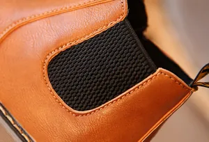 Macro detalle de bota de cuero marrón para niños con panel elástico negro lateral.