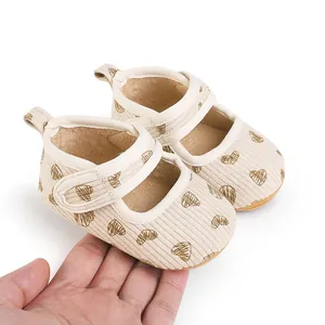 Close-up of beige baby walker shoes with heart patterns held in hand for size comparison
