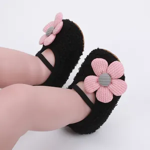Close-up of black fuzzy baby walking shoes featuring a large pink knitted flower detail.