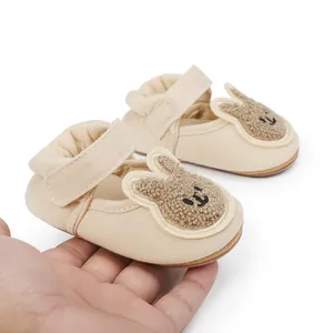 Vista detallada de zapatos de bebé beige con diseño de conejo sostenidos en la mano