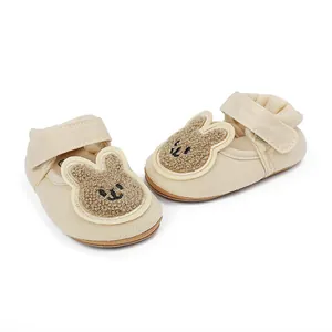 Detalle de zapatos beige para primeros pasos de bebé con parche de conejo.