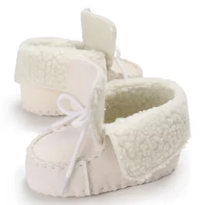 Dettaglio di scarpine neonato color crema con interno in pile e chiusura con lacci