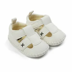 Detailed view of white textured faux leather baby sandals with black cross design.