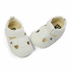 Detail shot of white faux leather baby sandals with velcro straps and X embroidery