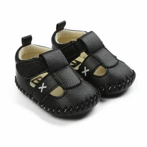 Close-up of black pebbled leather baby walking sandals with white X detail.