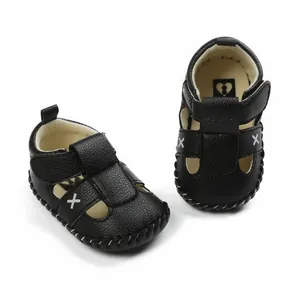 Detail of black faux leather baby sandals with white X embroidery and velcro strap.