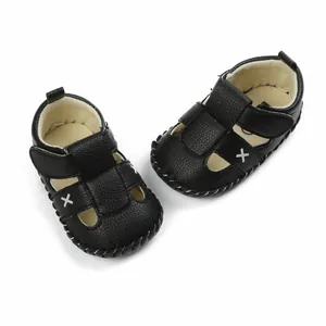 Detailed view of black faux leather baby sandals with white cross stitching accents