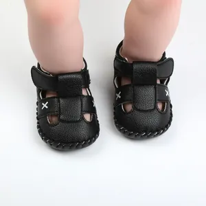 Detailed macro view of black faux leather baby sandals featuring white cross stitching