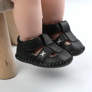 Close-up detail of black faux leather baby walking sandals with white cross stitch design