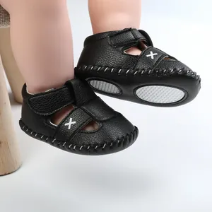 Close-up detail of black faux leather baby sandals with white cross stitch designs.