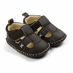 Macro view of dark brown faux leather baby sandals featuring white cross embroidery and stitching
