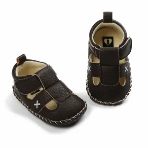 Detailed view of dark brown baby walking sandals featuring decorative white X embroidery