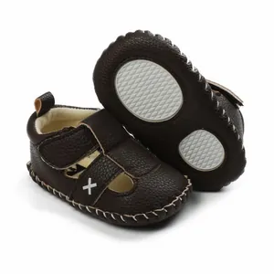 Detail of dark brown baby walker sandals with white cross mark and anti-slip sole.