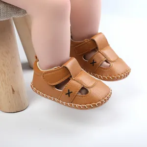 Detailed view of brown faux leather baby sandals with Velcro straps and cross design