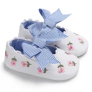 Détail de chaussures blanches bébé fille avec broderie florale rose et nœud rayé bleu