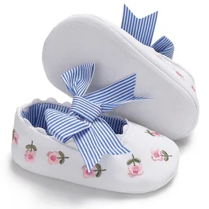 Gros plan de chaussures de marche pour bébé fille avec broderie florale et nœud rayé bleu