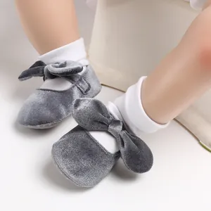 Close-up of grey velvet baby princess shoes with bows on a child's feet.
