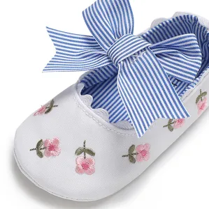 Détail d'une chaussure de princesse pour bébé fille avec broderie florale et nœud rayé bleu