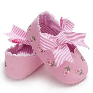 Gros plan de chaussures de princesse roses pour bébé avec broderie florale et nœud rayé.