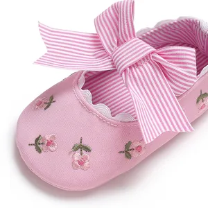 Gros plan de chaussure rose pour bébé fille avec broderie florale et grand nœud rayé