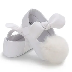 Gros plan de chaussures de princesse blanches pour bébé avec pompons doux et nœuds élégants.