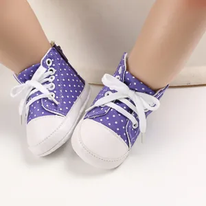Detail von lila gepunkteten Baby-Leinenschuhen mit weicher Sohle und weißen Schnürsenkeln.