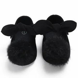 Détail de chaussures de princesse noires pour bébé avec de gros nœuds et pompons en fourrure.