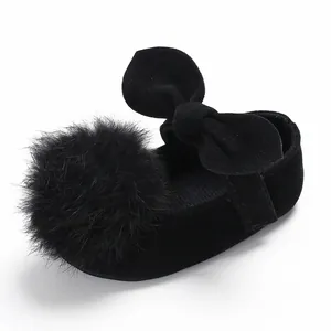 Détail d'une chaussure de princesse noire pour bébé avec grand pompon et nœud