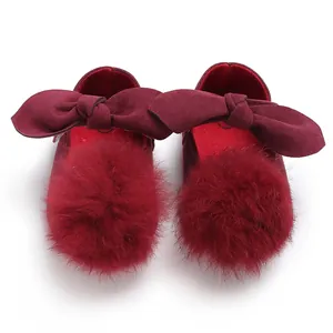 Gros plan de chaussures bébé bordeaux avec nœuds en velours et pompons en fausse fourrure