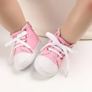 Makroansicht von rosa gepunkteten Segeltuch-Babyschuhen mit weißen Schnürsenkeln und weichen Sohlen