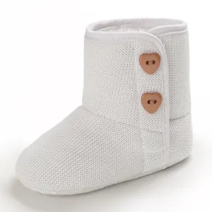 Gedetailleerde weergave van witte gebreide baby sneeuwlaarzen met houten hartknopen.