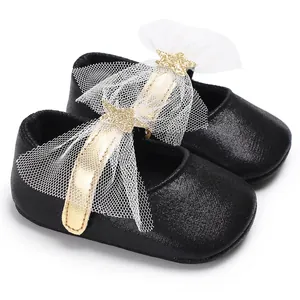 Nahaufnahme von schwarzen Baby-Prinzessin-Schuhen mit Goldriemen und Netzbogendetail.