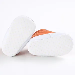 Detailed macro view of the non-slip white soft sole texture on orange baby walker shoes