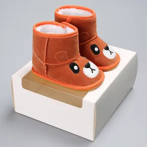 Side view of cute brown baby winter boots with bear design resting on a white gift box
