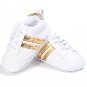 Primer plano de los zapatos blancos para bebé con elegantes y modernas rayas doradas.