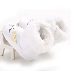 Detail view of white baby winter snow boots with soft faux fur lining and yellow bow
