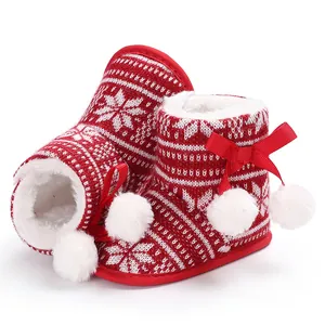 Close-up of red Christmas baby winter boots with snowflake pattern and pom-poms.