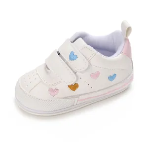 Detail of white baby sneakers with colorful embroidered hearts and velcro straps.