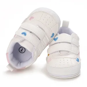 Detail shot of white baby sneakers featuring colorful heart embroidery and velcro straps.