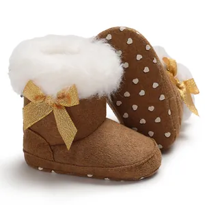 Close-up detail of brown baby winter boots with white faux fur trim and a shiny gold bow