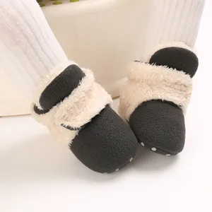 Primer plano de botas de nieve para bebé en felpa negra con borde crema y suela blanda